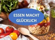 Foto in der Mitte in blauem Oval: Essen macht glücklich, im Hintergrund gedeckter Tisch mit Äpfeln, einem Glas mit Nüssen,...